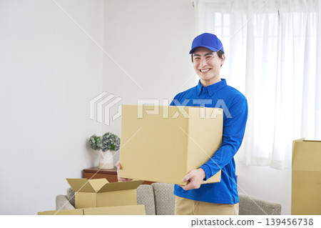 A smiling moving company worker holding cardboard boxes. 139456738