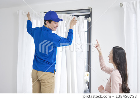 搬家公司人員一邊安裝窗簾，一邊聽一位女士講解。 139456758