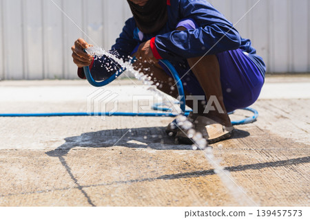 Construction worker wash down concrete surface with a water hose. Construction worker wash down concrete surface with a water hose. 139457573