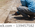 A construction worker using power drill to bore into a concrete curb. 139457582