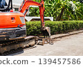 An orange crawler excavator digs a trench along a paved residential road for maintenance. 139457586