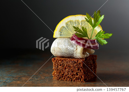 Rye bread canape with herring filet, red onion, lemon, and parsley. Rye bread canape with herring filet, red onion, lemon, and parsley. 139457767