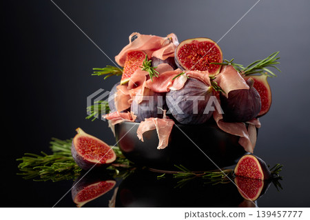 Prosciutto with rosemary and fig fruit on a black reflective background. Prosciutto with rosemary and fig fruit on a black reflective background. 139457777