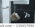 Close-up of a shower loofah hanging on a metal hook against black tile wall. 139457894