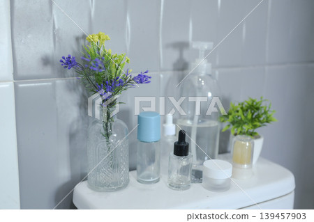 Minimalist bathroom decor with assorted toiletries and floral arrangement against a tiled wall. 139457903