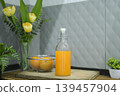 Refreshing cold orange juice bottle and glass with citrus fruits against a grey tile background. 139457904