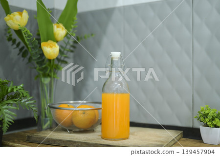 Refreshing cold orange juice bottle and glass with citrus fruits against a grey tile background. Refreshing cold orange juice bottle and glass with citrus fruits against a grey tile background. 139457904