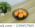 Fresh oranges in a black wire mesh fruit bowl on a wooden table. 139457905