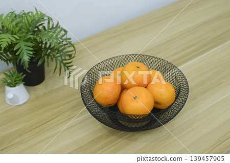 Fresh oranges in a black wire mesh fruit bowl on a wooden table. Fresh oranges in a black wire mesh fruit bowl on a wooden table. 139457905