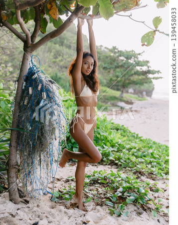 Beauty woman in bikini posing on sandy beach with fishing net, looking at camera Beauty woman in bikini posing on sandy beach with fishing net, looking at camera 139458033