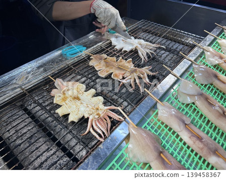 Filming vendors skillfully preparing grilled squid at a night market in Taichung. Filming vendors skillfully preparing grilled squid at a night market in Taichung. 139458367