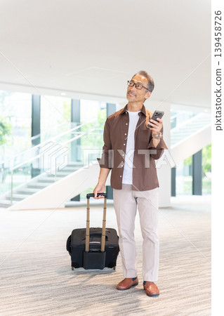 一位老年男性旅客入住飯店,透過智慧型手機預訂。 一位老年男性旅客入住飯店,透過智慧型手機預訂。 139458726