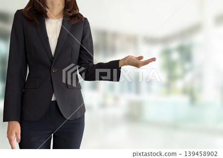 A woman in a suit raises her palm to introduce herself. 139458902