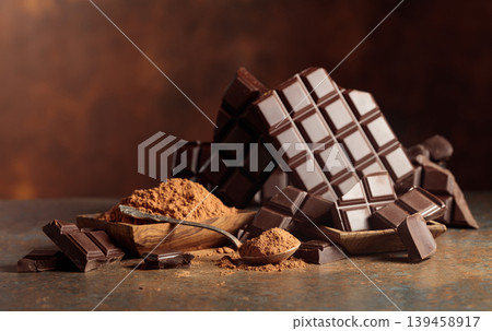 Scraps of dark chocolate next to a wooden bowl of cocoa powder. 139458917
