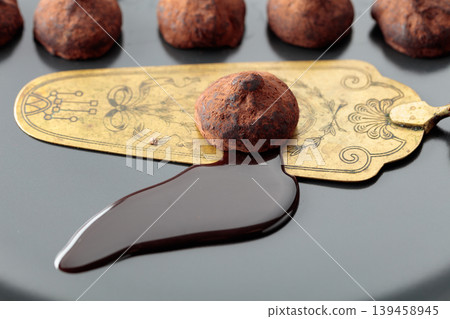 Chocolate truffles, chocolate sauce, and vintage brass cake server on a black plate. Chocolate truffles, chocolate sauce, and vintage brass cake server on a black plate. 139458945