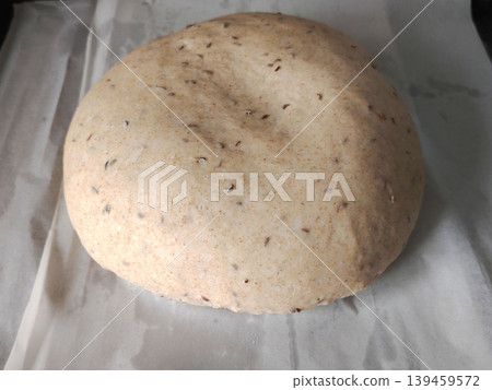 Raw sourdough bread dough with caraway seeds resting on white parchment paper before baking. Raw sourdough bread dough with caraway seeds resting on white parchment paper before baking. 139459572
