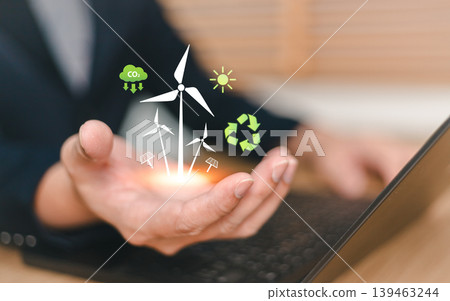 Close up of businessman hand holding virtual renewable energy icons with wind turbines and solar cells. Concept of sustainable ecological solution, green technology and environmental conservation Close up of businessman hand holding virtual renewable energy icons with wind turbines and solar cells. Concept of sustainable ecological solution, green technology and environmental conservation 139463244