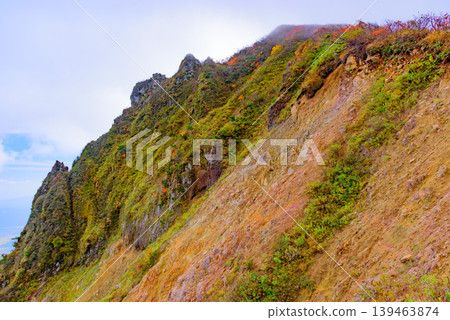 The rugged rock faces of Mount Bandai and the vibrant autumn foliage: Autumn mountain scenery visible from the hiking trail from the trailhead. Fukushima Prefecture. The rugged rock faces of Mount Bandai and the vibrant autumn foliage: Autumn mountain scenery visible from the hiking trail from the trailhead. Fukushima Prefecture. 139463874