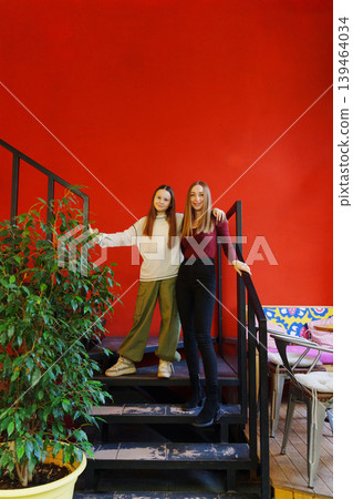 Friends pose on stairs in a colorful cafe setting with plants 139464034