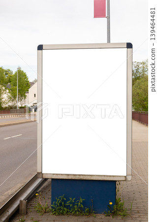 An empty advertising board is located on the side of the road in a quiet neighborhood. No advertisements are shown and nearby plants grow at the base of the board 139464481