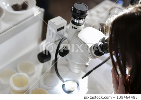 Person observing a sample in a petri dish under a binocular microscope, illustrating scientific research in a lab. Person observing a sample in a petri dish under a binocular microscope, illustrating scientific research in a lab. 139464483