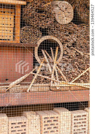 A structure made of wood and natural items stands in a garden. It serves as a home for insects like bees and ladybugs. The design includes various materials placed together A structure made of wood and natural items stands in a garden. It serves as a home for insects like bees and ladybugs. The design includes various materials placed together 139464527