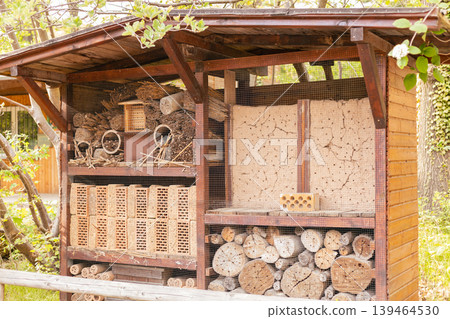 An insect hotel stands in a garden, designed to offer shelter for insects. It is made from wood, sticks, and natural materials. The structure is full of different sections for various insects An insect hotel stands in a garden, designed to offer shelter for insects. It is made from wood, sticks, and natural materials. The structure is full of different sections for various insects 139464530