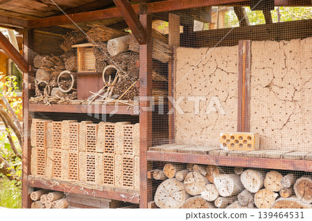 The insect hotel stands in a garden, built with wood and clay. It offers habitat for bees, beetles, and other insects to nest and find shelter. The structure is organized in sections The insect hotel stands in a garden, built with wood and clay. It offers habitat for bees, beetles, and other insects to nest and find shelter. The structure is organized in sections 139464531