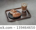 A wooden tray holds a refreshing iced latte in a textured glass, paired with two spinach and ham truffle salad rolls served on a decorative black plate. 139464650
