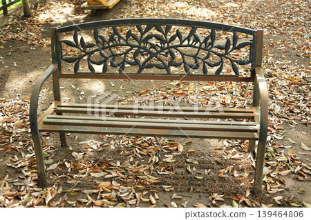 A cast iron bench with a plant motif stands in the park, surrounded by a carpet of fallen leaves. A cast iron bench with a plant motif stands in the park, surrounded by a carpet of fallen leaves. 139464806