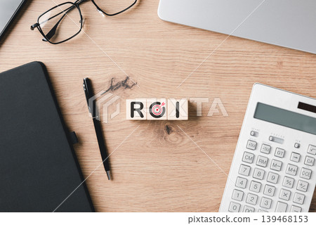 ROI return on investment concept featuring wooden blocks on an office desk with calculator and notebook to represent financial growth, profit analysis, and successful business goal marketing. 139468153