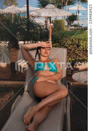 Beauty woman resting on lounge chair with radiant bronzed healthy summer complexion outdoors today. Beautiful female displaying smooth glowing skin texture during tropical vacation relaxation beside Beauty woman resting on lounge chair with radiant bronzed healthy summer complexion outdoors today. Beautiful female displaying smooth glowing skin texture during tropical vacation relaxation beside 139468425