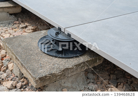 Close-up of adjustable pedestal support for raised terrace flooring. Installed on gravel base for stability and drainage. Close-up of adjustable pedestal support for raised terrace flooring. Installed on gravel base for stability and drainage. 139468628