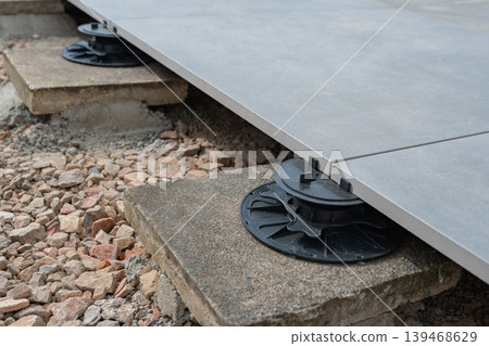 Structural detail of a raised deck supported by adjustable pedestals on gravel. The system allows airflow and prevents moisture damage in outdoor flooring installations. Structural detail of a raised deck supported by adjustable pedestals on gravel. The system allows airflow and prevents moisture damage in outdoor flooring installations. 139468629