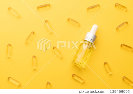 Oil capsules and serum bottle with dropper on yellow background. Nutritional supplement contains fish oil, omega 3, omega 6, omega 9, vitamin e, vitamin d and vitamin. Health care and beauty concept. Oil capsules and serum bottle with dropper on yellow background. Nutritional supplement contains fish oil, omega 3, omega 6, omega 9, vitamin e, vitamin d and vitamin. Health care and beauty concept. 139469005