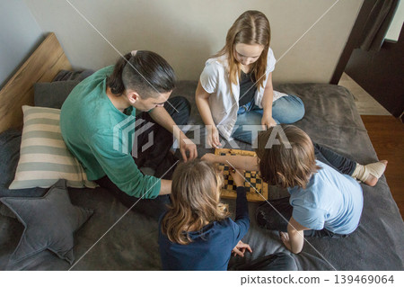 Four people gather in a room, sitting on a bed. They focus on a tablet while one person Four people gather in a room, sitting on a bed. They focus on a tablet while one person 139469064