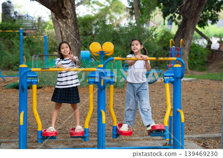 Two Asian student girls exercising together on outdoor fitness equipment at the school playground, Back to school and healthy lifestyle concept. Two Asian student girls exercising together on outdoor fitness equipment at the school playground, Back to school and healthy lifestyle concept. 139469230