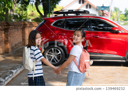 Two Asian student girls with backpacks holding hands and walking to the car to go home after school, Back to school and family transportation concept. Two Asian student girls with backpacks holding hands and walking to the car to go home after school, Back to school and family transportation concept. 139469232