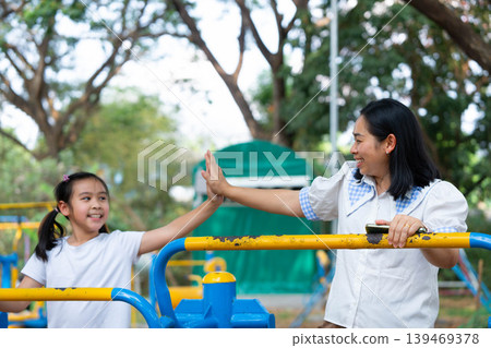 Asian mother and daughter exercising together on outdoor fitness equipment at the school playground, Back to school and healthy lifestyle concept. Asian mother and daughter exercising together on outdoor fitness equipment at the school playground, Back to school and healthy lifestyle concept. 139469378