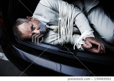 Car boot, crime and portrait of business man with tape, rope and kidnap danger in parking lot. Fear, stress and face of male victim in a vehicle trunk with anxiety, horror or panic, scared or ransom Car boot, crime and portrait of business man with tape, rope and kidnap danger in parking lot. Fear, stress and face of male victim in a vehicle trunk with anxiety, horror or panic, scared or ransom 139469992