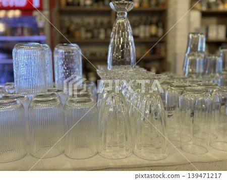 Upside-down glassware set on shelf in bar or restaurant with various drink bottles in background Upside-down glassware set on shelf in bar or restaurant with various drink bottles in background 139471217
