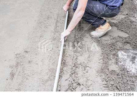 Worker leveling concrete with screed for slab foundation Worker leveling concrete with screed for slab foundation 139471564