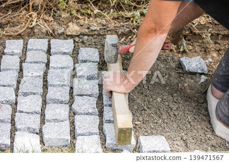 Worker aligning cobblestone paving stones with hammer 139471567
