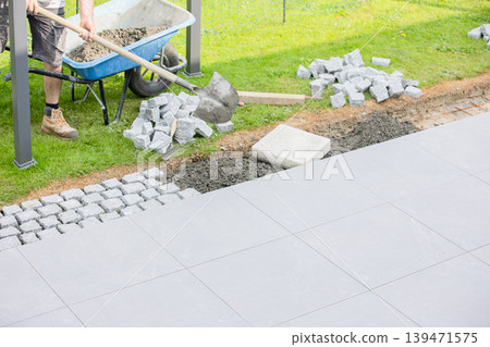 Construction worker preparing base for cobblestone pavement installation with shovel 139471575