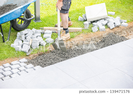 Construction worker preparing base for cobblestone pavement installation with shovel Construction worker preparing base for cobblestone pavement installation with shovel 139471576