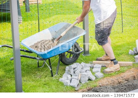 Construction worker preparing base for cobblestone pavement installation with shovel Construction worker preparing base for cobblestone pavement installation with shovel 139471577
