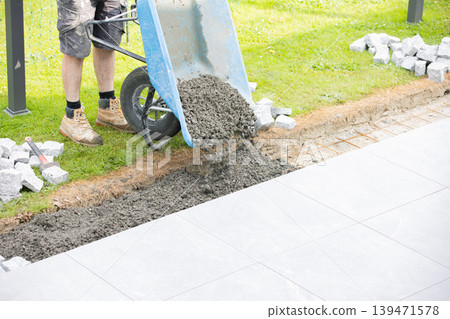 Construction worker pouring concrete from wheelbarrow for pavement installation Construction worker pouring concrete from wheelbarrow for pavement installation 139471578