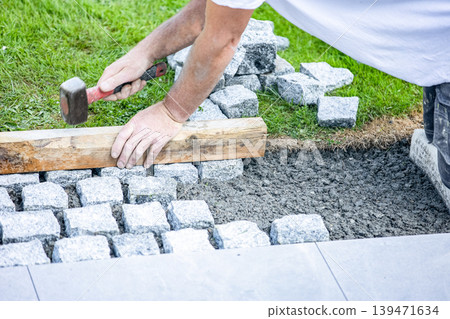 Worker installing cobblestone pavement with hammer and wooden guide 139471634