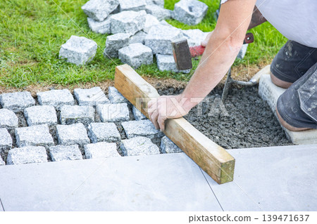 Worker installing cobblestone pavement with hammer and wooden guide 139471637
