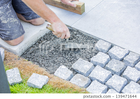 Construction worker installing cobblestone pavement with trowel on garden walkway Construction worker installing cobblestone pavement with trowel on garden walkway 139471644